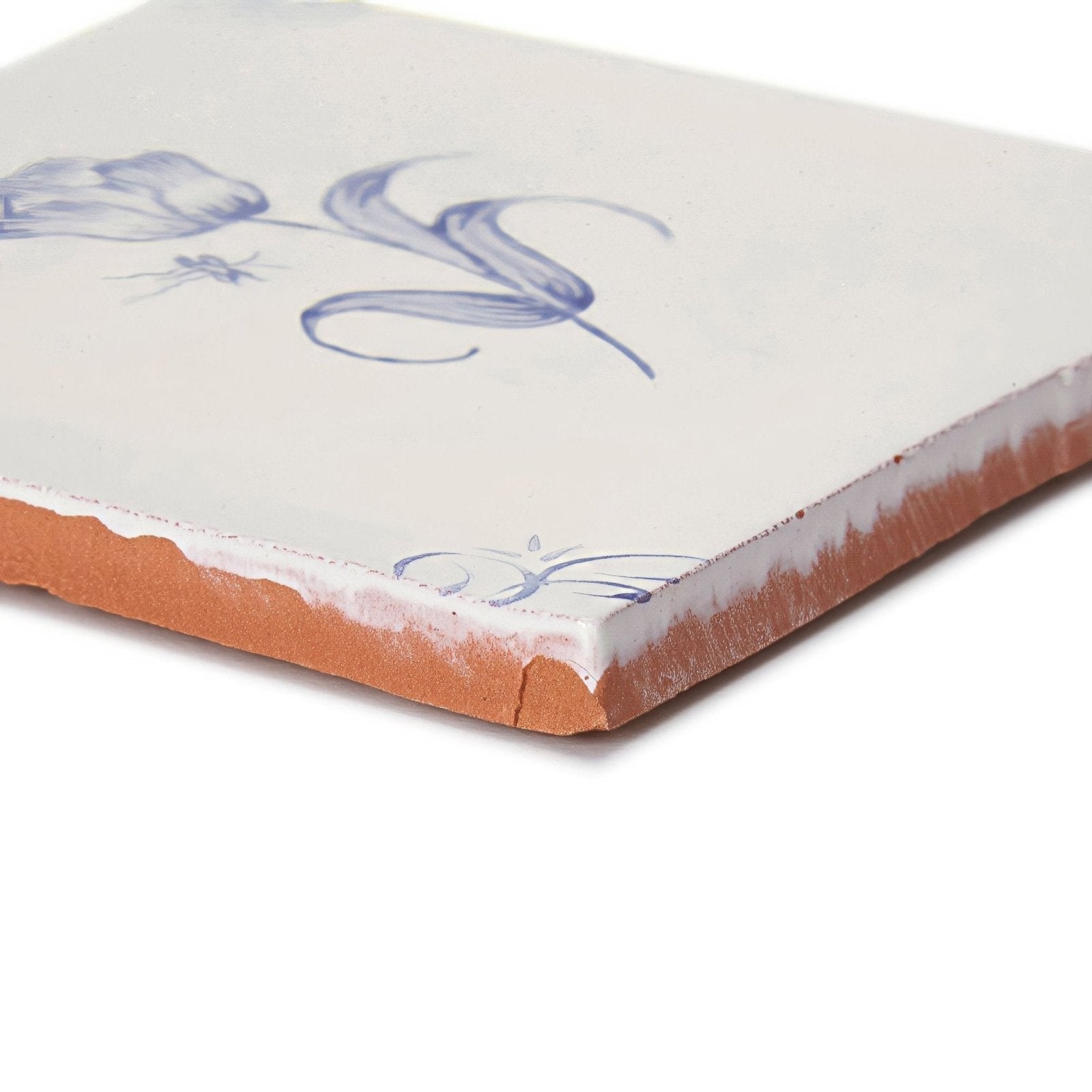 A square english delft tulip blue gloss ceramic tile with white glaze blue floral design and terracotta edge visible