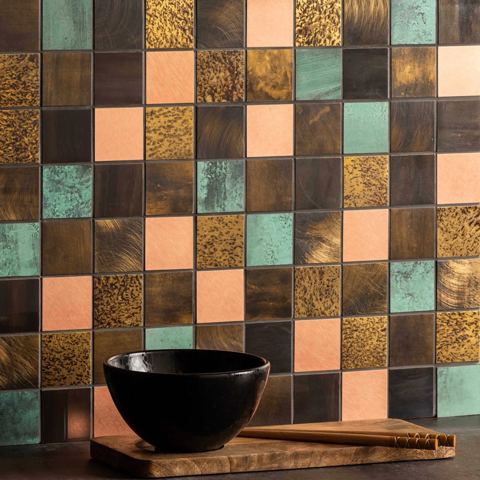 Black ceramic bowl with mixed copper mosaic design resting on a wooden cutting board for serving and decor