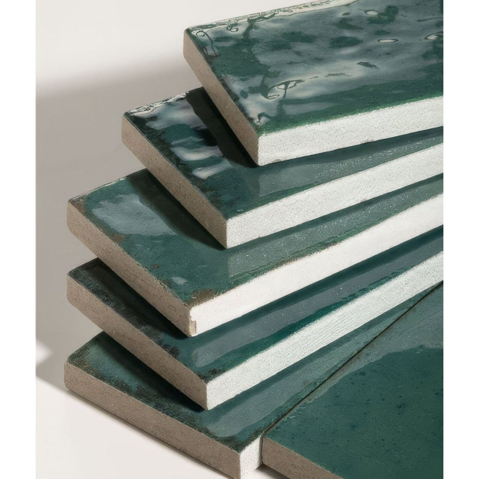 Stacked rectangular foundry novo porcelain tiles with glossy deep teal glaze and textured white edges in irish green color