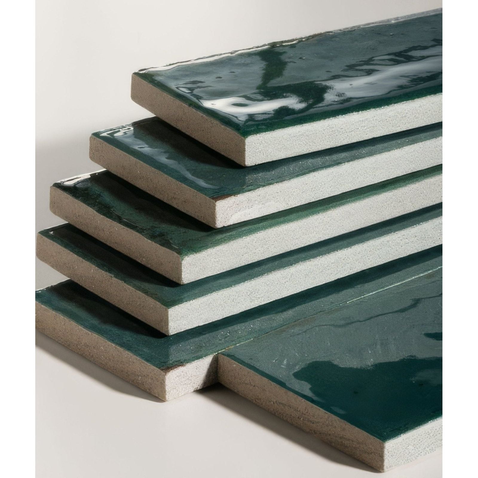 Stacked rectangular foundry novo porcelain tiles with glossy deep green glaze and textured light gray concrete edges