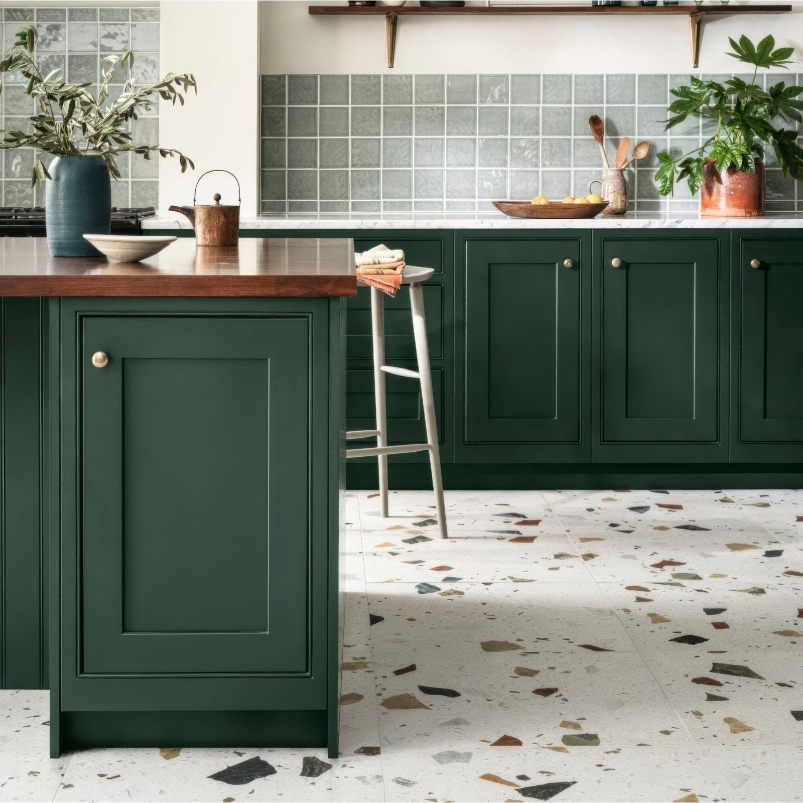 Deep green shaker-style kitchen cabinets with raised panel doors and round brass knobs featuring frammento multi terrazzo effect porcelain tile