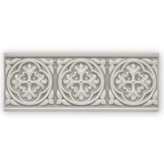 A rectangular off-white ceramic tile giralda niebla grey border with three raised floral medallions and leafy patterns