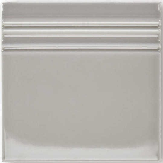 A sleek square ceramic giralda niebla grey skirting tile with a smooth glossy finish and three horizontal ridges near the top