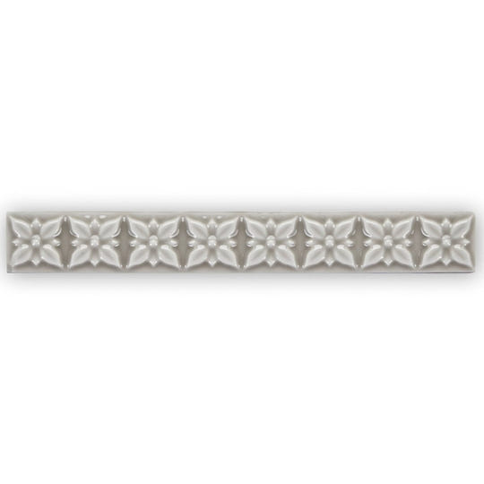 Giralda Niebla Grey Trim sleek off-white ceramic tile strip with embossed five-petaled floral pattern and central dots