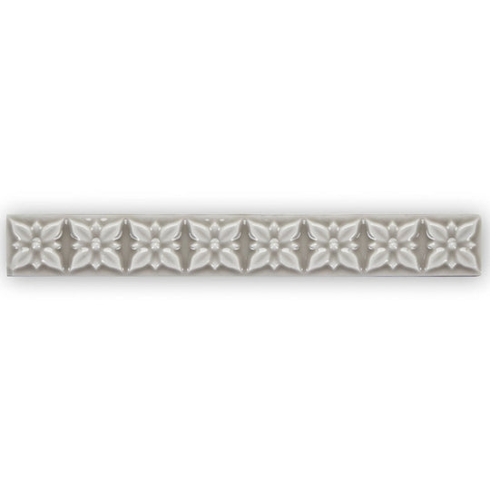 Giralda Niebla Grey Trim sleek off-white ceramic tile strip with embossed five-petaled floral pattern and central dots