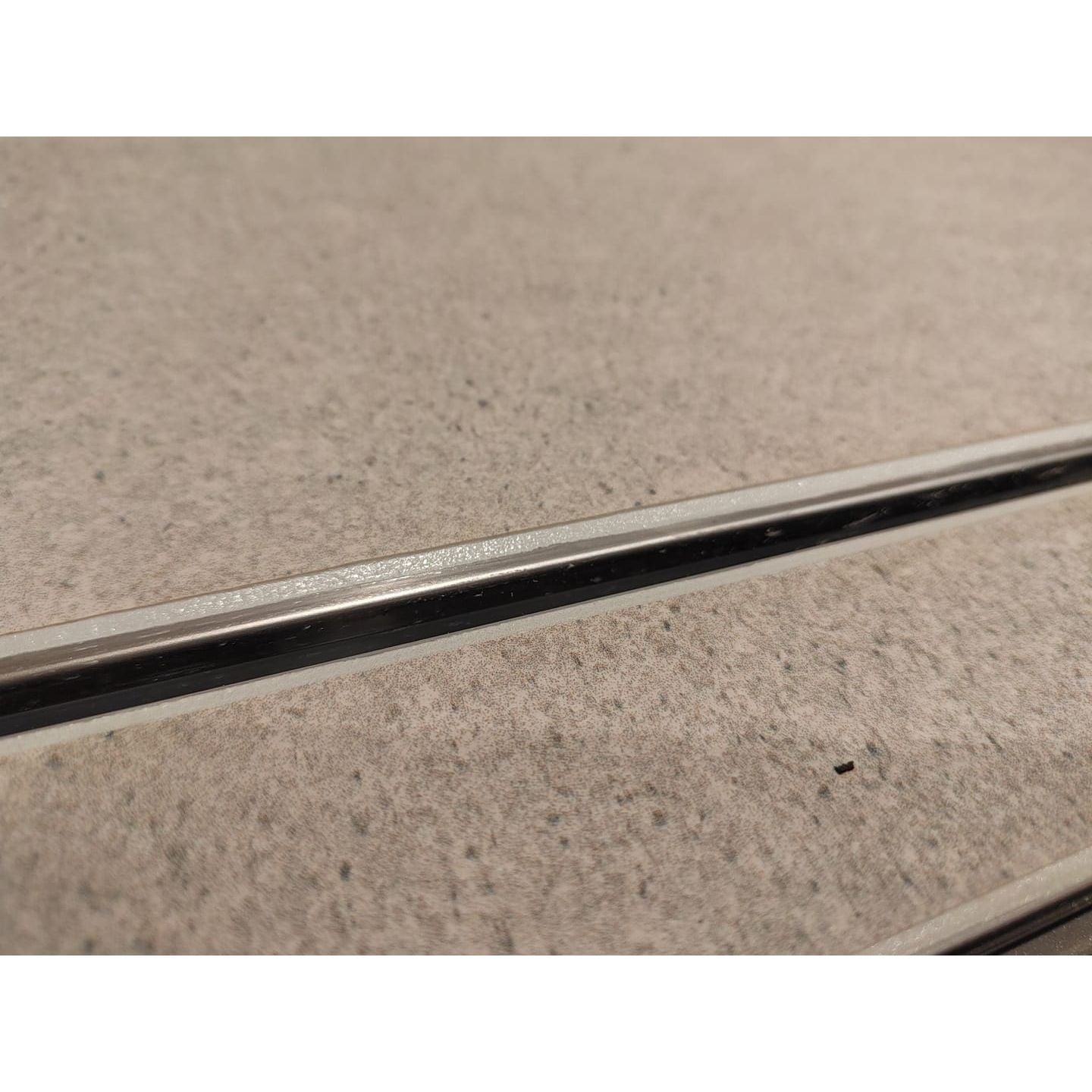 A sleek metallic silver strip with a polished finish on textured beige surface for GoPoxy epoxy grout edges