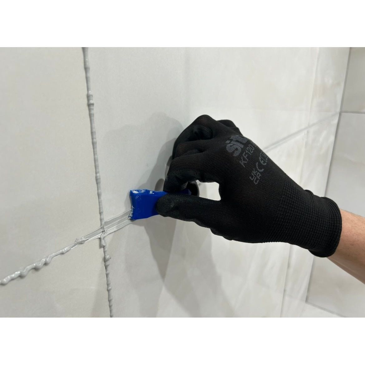 Blue silicone caulk gun applying white epoxy grout between tiled surfaces using GoPoxy epoxy grout product