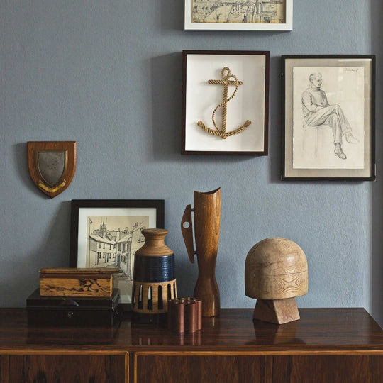 Graphite rustic wooden anchor sculpture made from twisted rope in dark brown frame against light blue wall