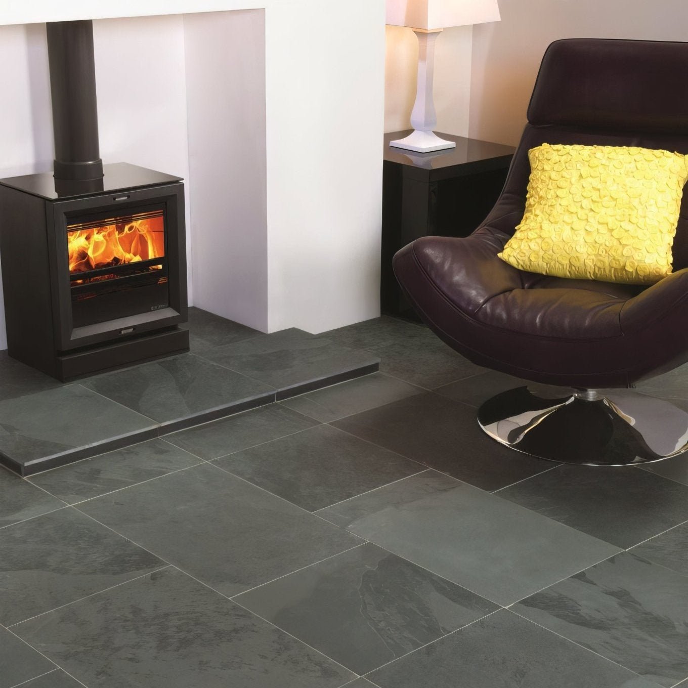 Black wood-burning stove with glass front showing glowing orange flames on graphite black natural slate 600 x 400mm