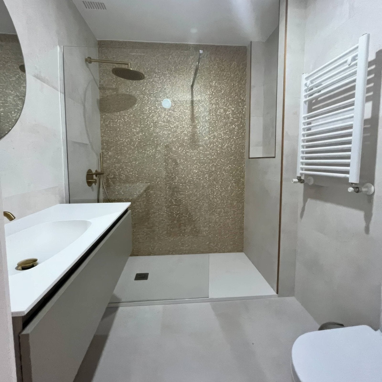 The gravity aluminium hexagon gold mosaic tiles clad a shower wall with brass fixtures and a glass enclosure