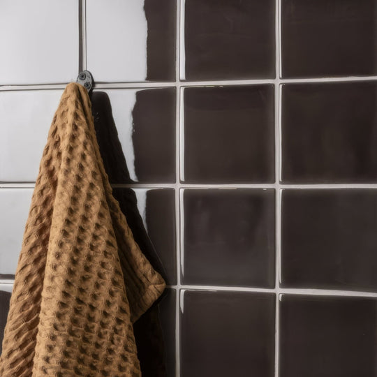 A tan waffle-weave towel hanging from a hook against dark grey field tile background