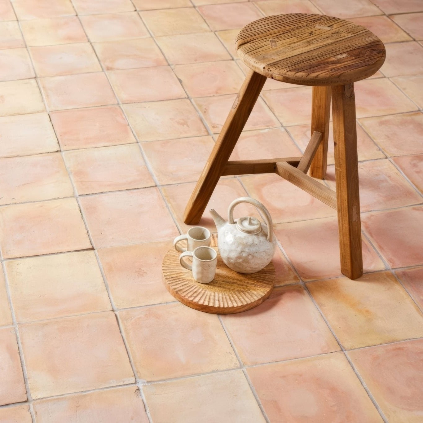A rustic wooden stool with a round slatted seat and three angled legs beside handmade classic terracotta square tile 30.5x30.5cm