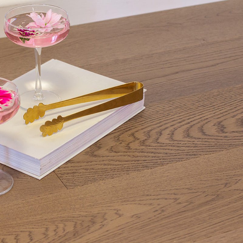 Gold-colored metal tongs with leaf-shaped ends resting on white paper for harlech biscotti oak display