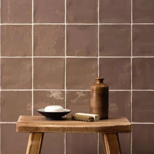 A matte brown ceramic hessian field tile vase with a narrow neck sits on a rustic wooden stool