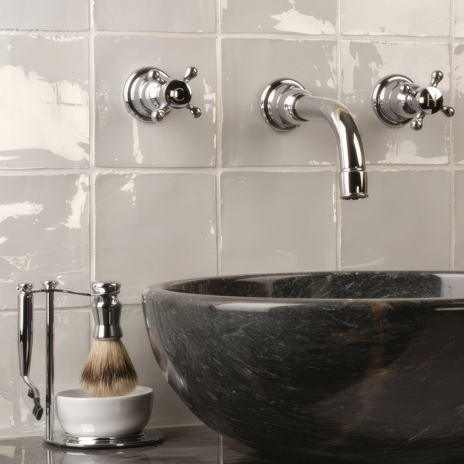 Chrome-finished wall-mounted faucet with curved spout and cross handles on light gray hibiscus field tile wall