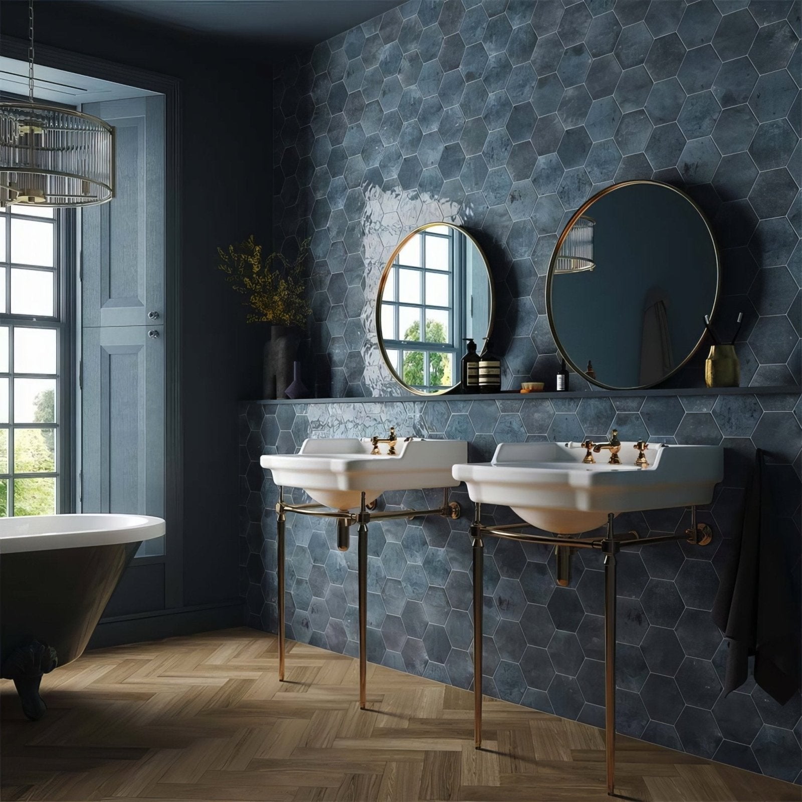 Two white ceramic pedestal sinks with brass legs and fixtures against a dark blue hope blue hexagon gloss ceramic wall