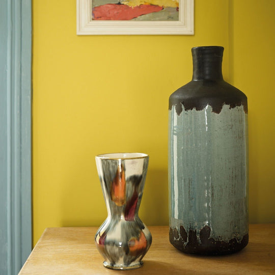 A sleek metallic silver hourglass vase with a reflective surface beside a taller ceramic vessel hustle at 5pm