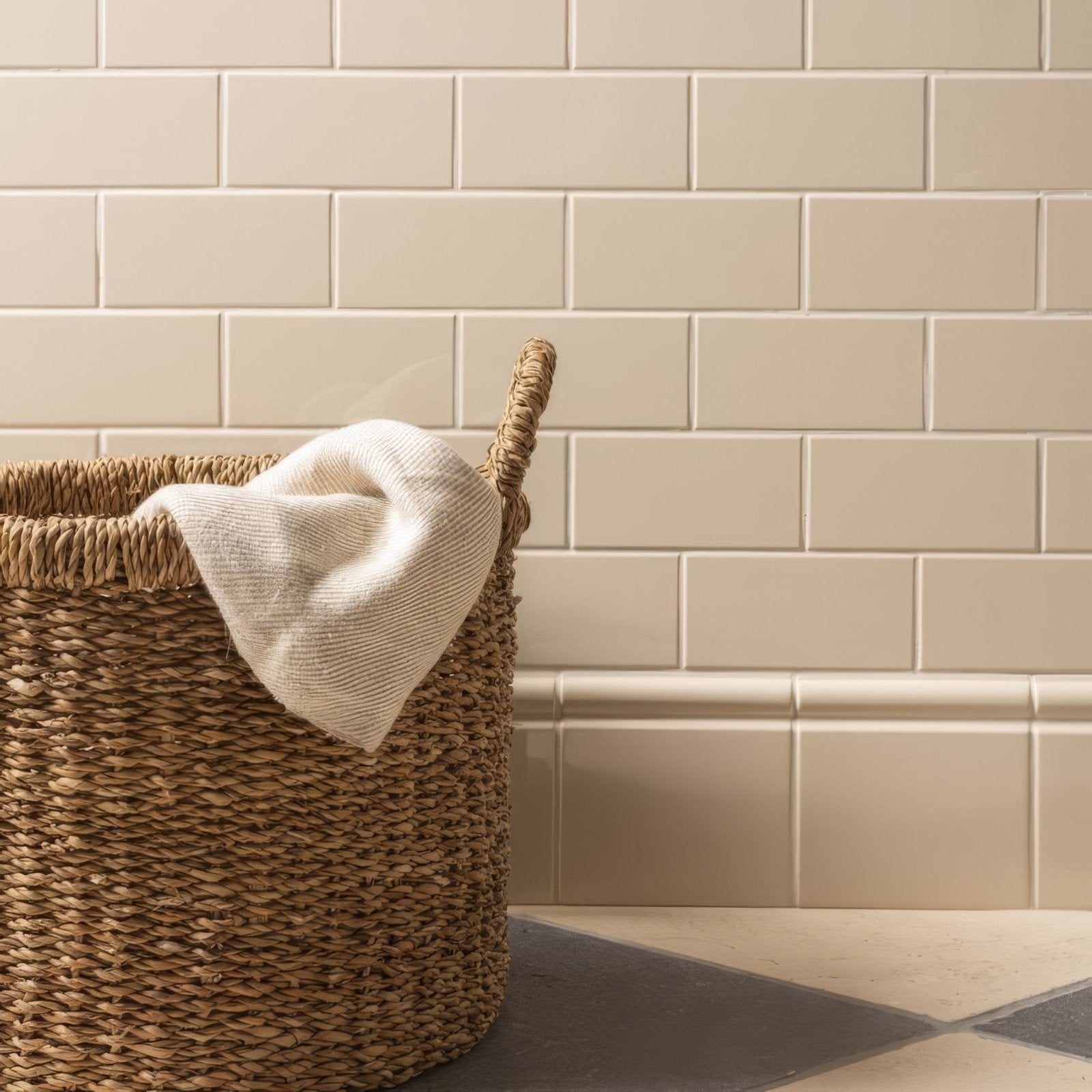 Woven natural fiber ivory half tile laundry basket with sturdy handle holding soft off-white towel