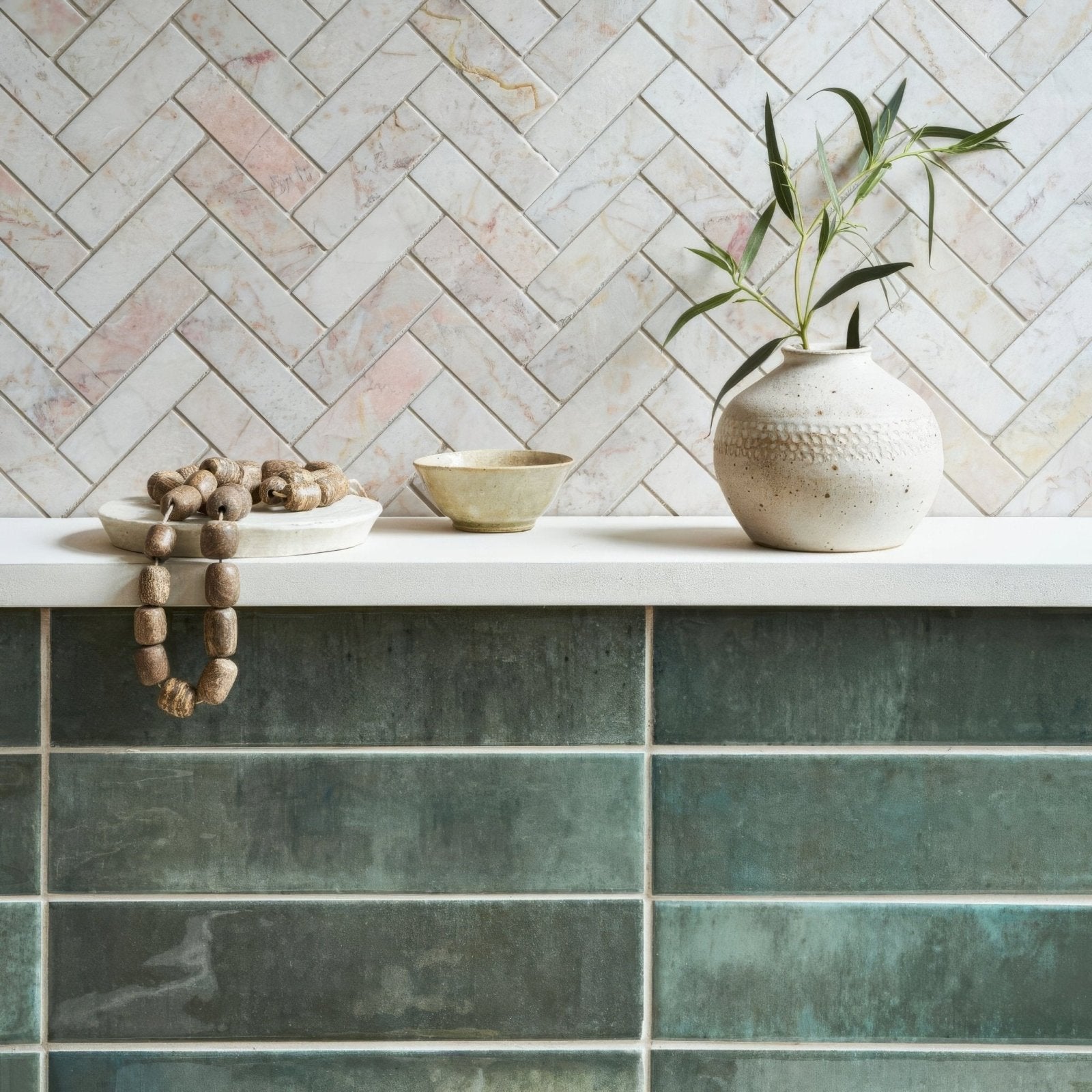 A textured off-white ceramic vase with speckled finish and embossed pattern holding green leaves beside an ixworth forest brick tile