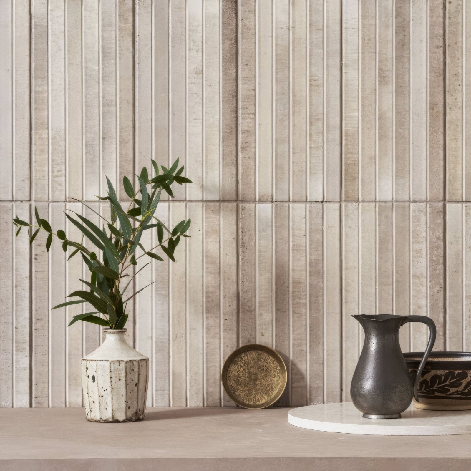 A white speckled ceramic vase with a geometric faceted design holding green eucalyptus branches on ixworth ivory bar tile