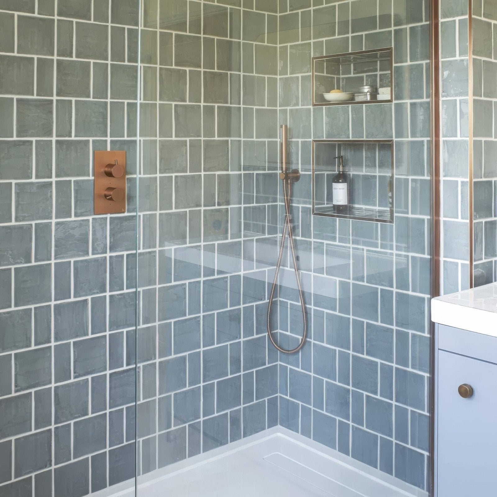 Modern copper finished shower faucet with sleek minimalist design paired with jaipur dartmouth green square glazed tile