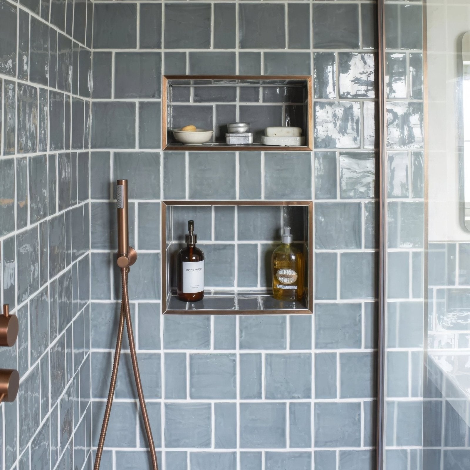 Copper-framed recessed shower shelves with glass fronts holding toiletries against gray tiled walls with jaipur dartmouth green square glazed tile