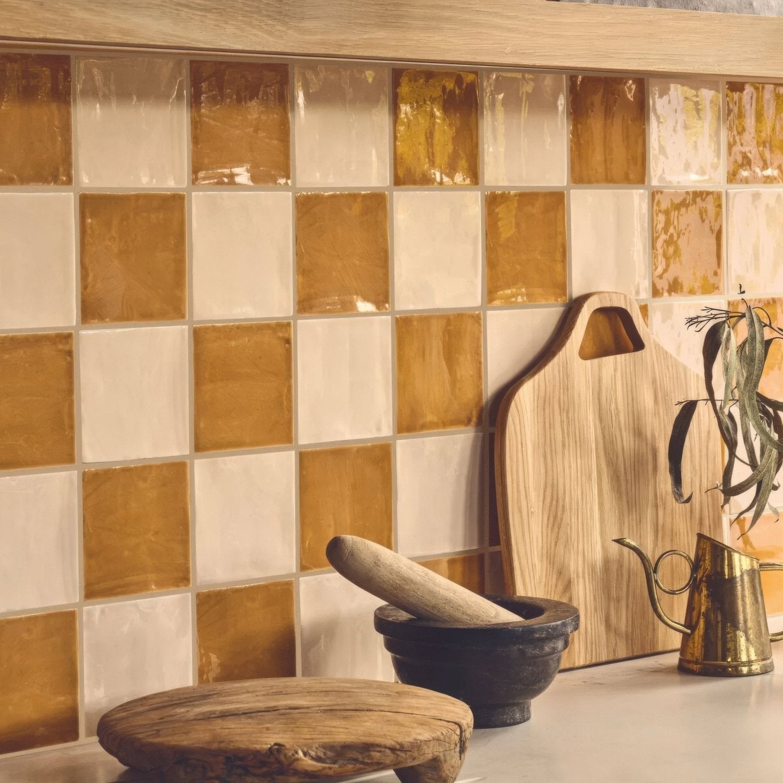 A rustic wooden Jaipur Hoppers hat square glazed tile cutting board with natural grain and handle cutout leaning on wall