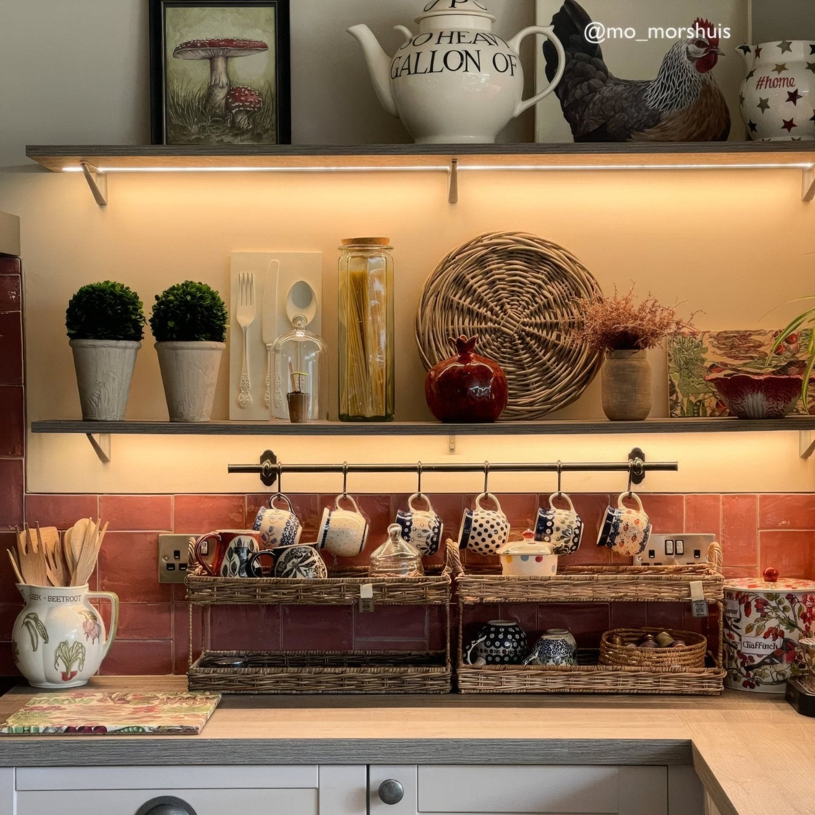 Jaipur pompeiian red square glazed tile displayed on a woven wicker shelf with ceramic mugs and pasta jar
