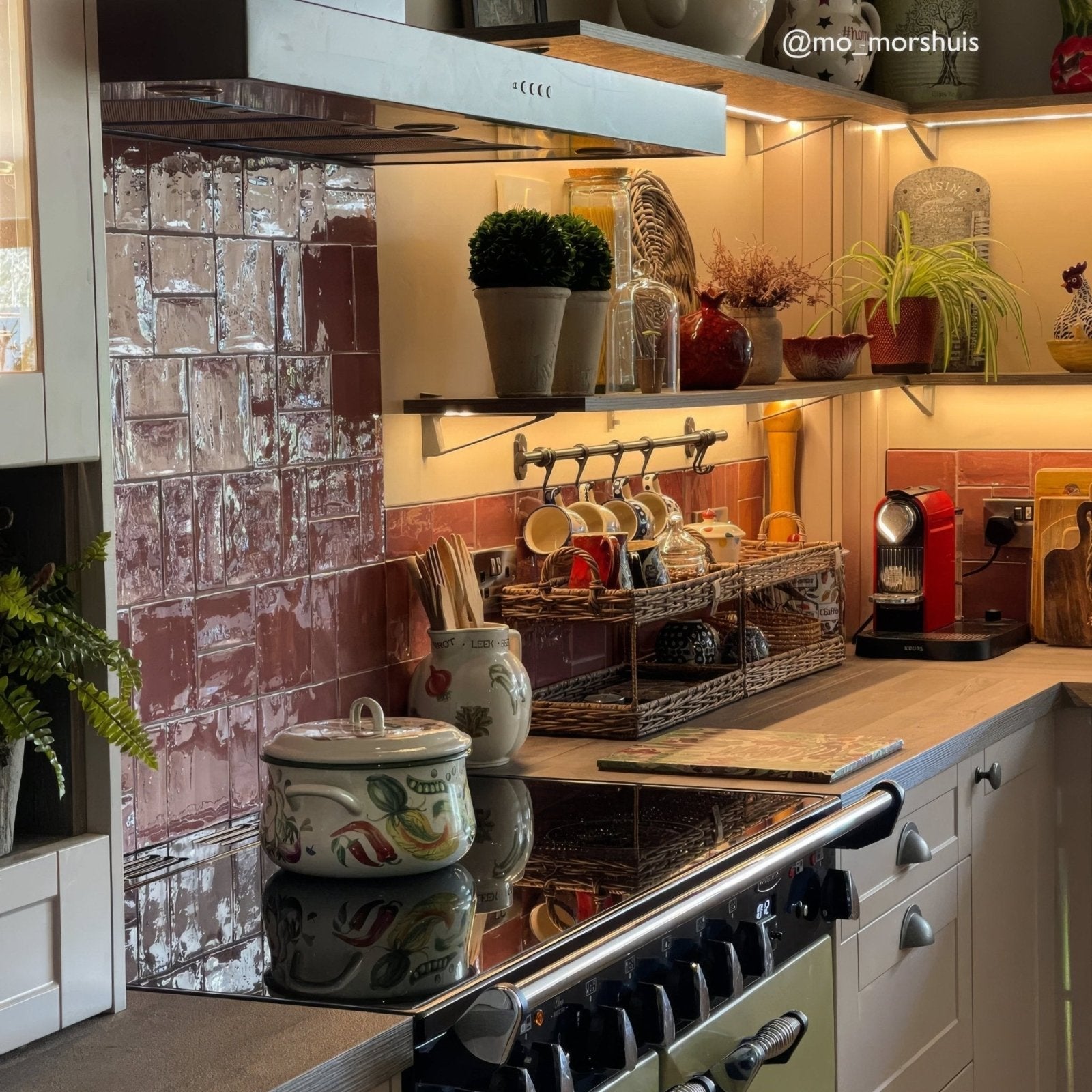 A white ceramic pot with floral pattern and lid on a stovetop alongside jaipur pompeian red square glazed tile