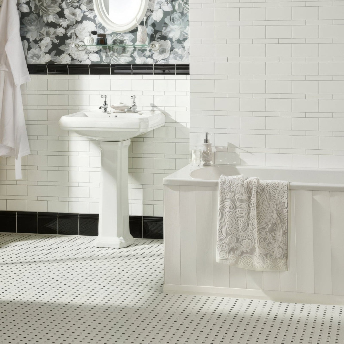White pedestal sink with chrome faucets installed above jet black ceramic skirting tile in modern bathroom setting