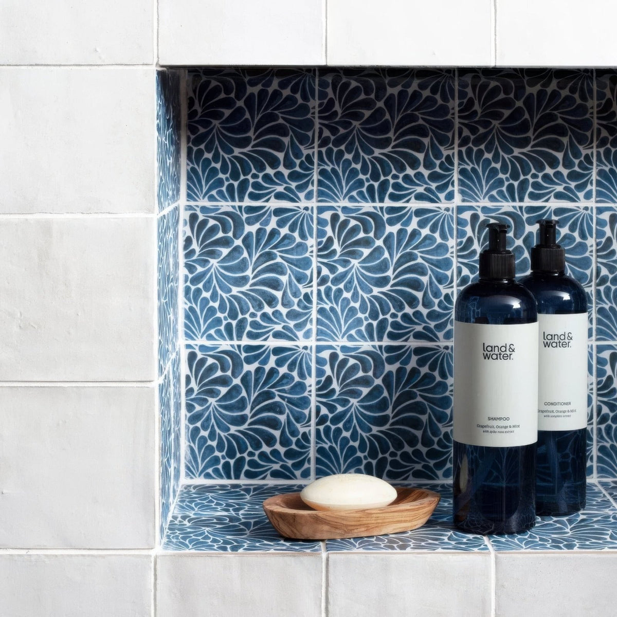 Two dark blue glass bottles with black pumps and land & water labels on kelmscott emery blue patterned tile shelf