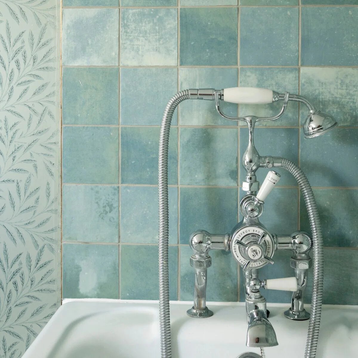Chrome-finished vintage-style bathtub faucet with white ceramic handles and matching showerhead against kelmscott green tile