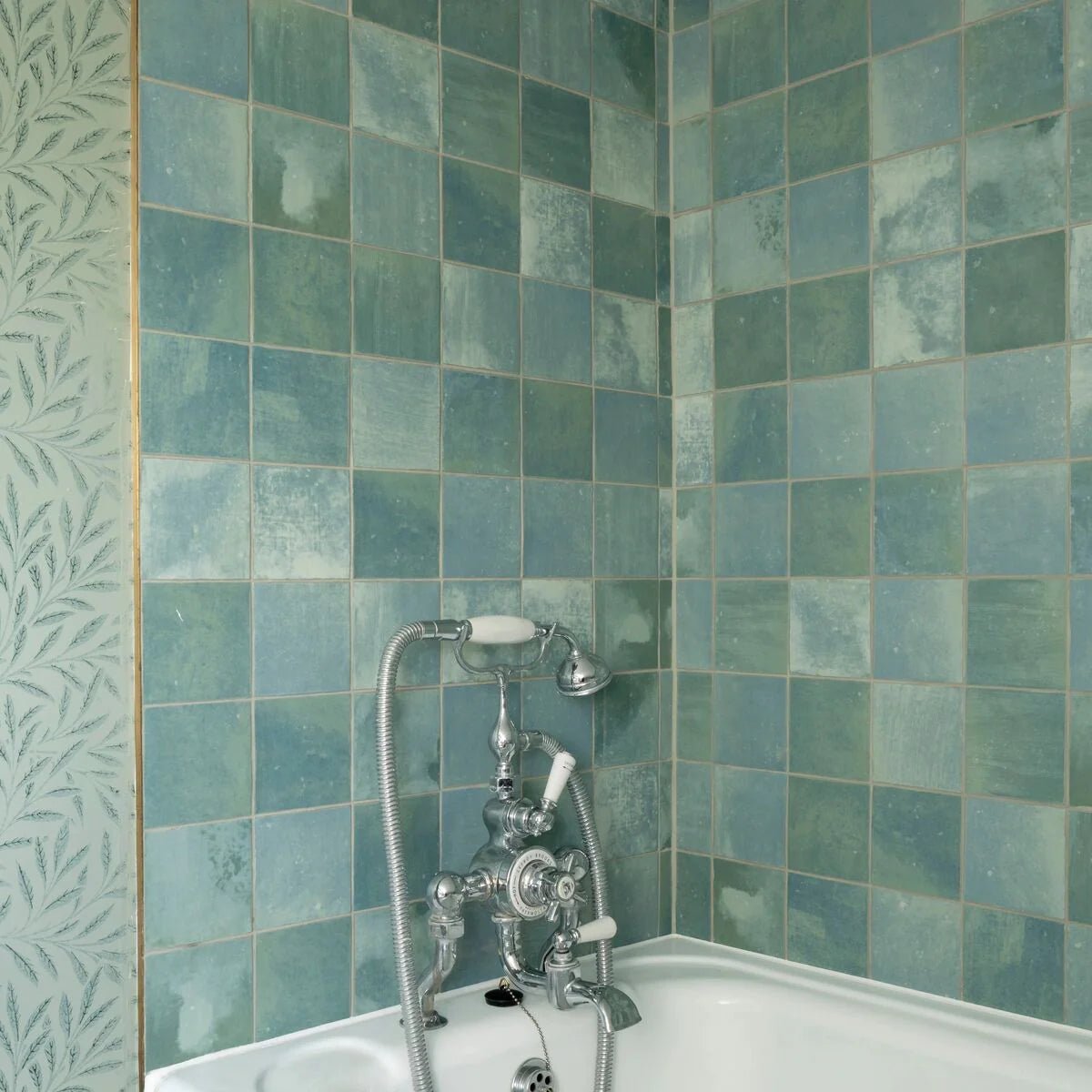 Antique-style chrome bathtub faucet with white ceramic handles and flexible hose against kelmscott green tile walls