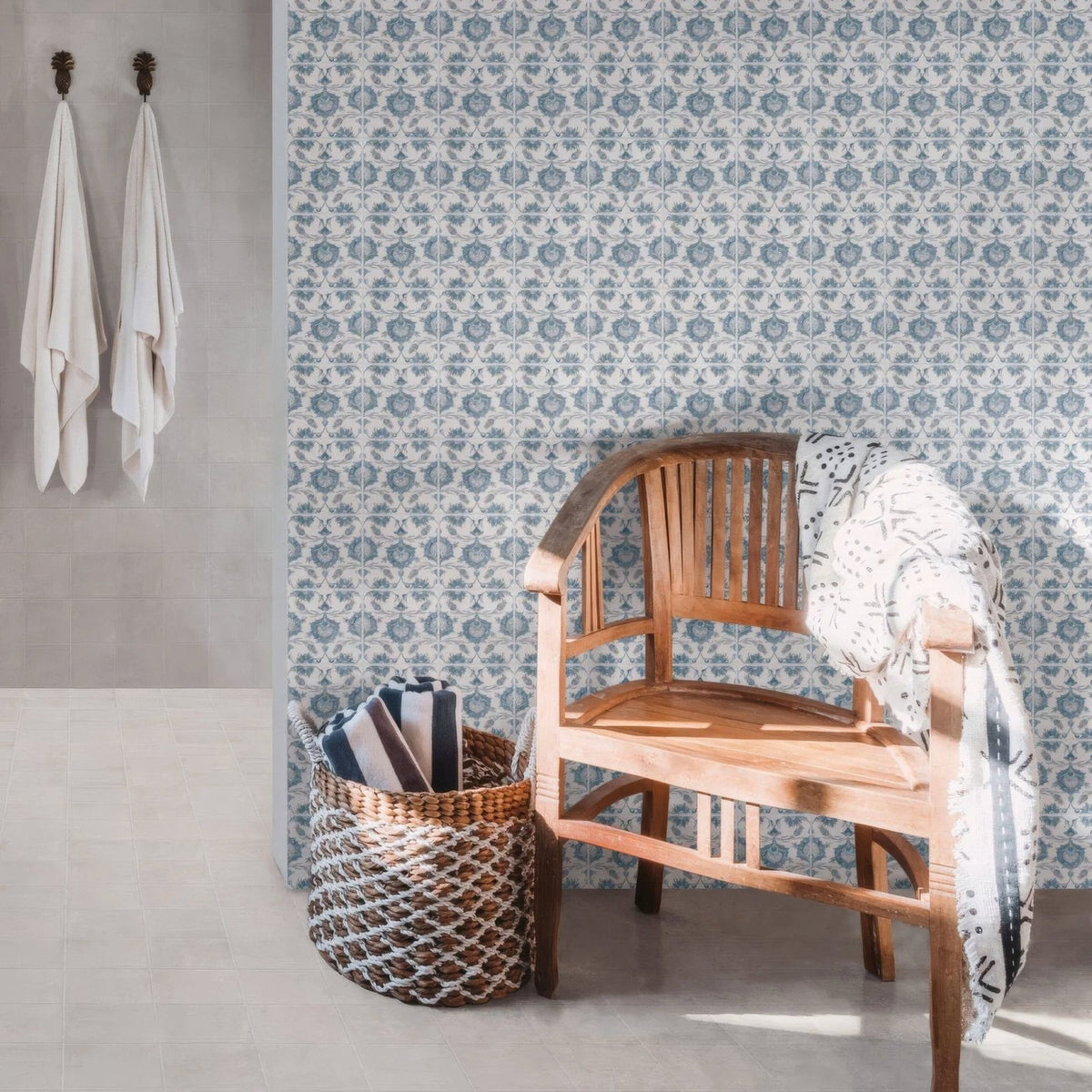 A light brown wooden chair with slatted back and curved armrests draped with a white blanket and kelmscott standen blue patterned tile