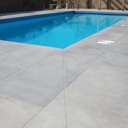Rectangular kimmeridge limestone pool with etched finish clear blue water and dark blue mosaic tiled edge
