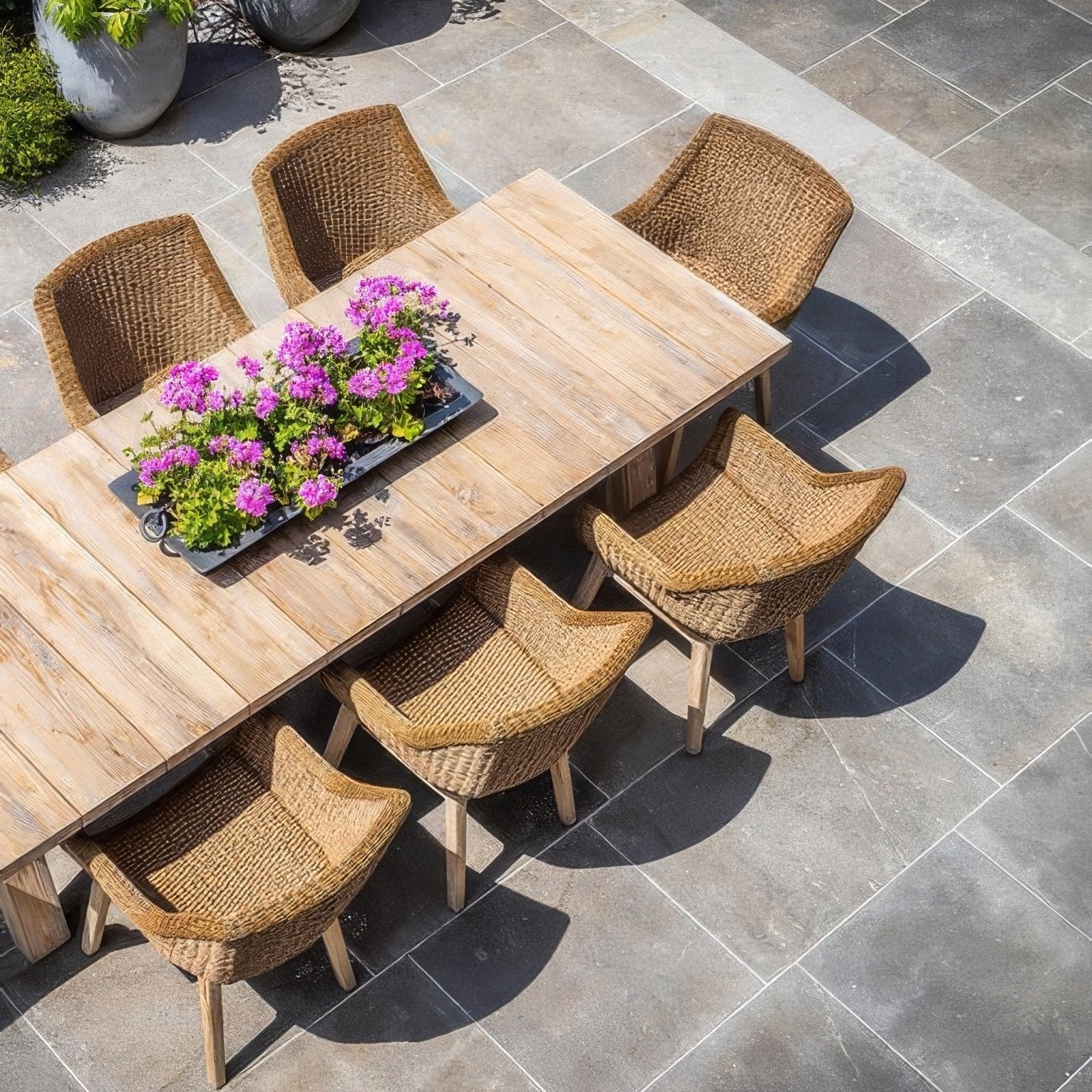 Light brown woven wicker dining set with wooden table and matching chairs on kimmeridge limestone paving tumbled and etched finish