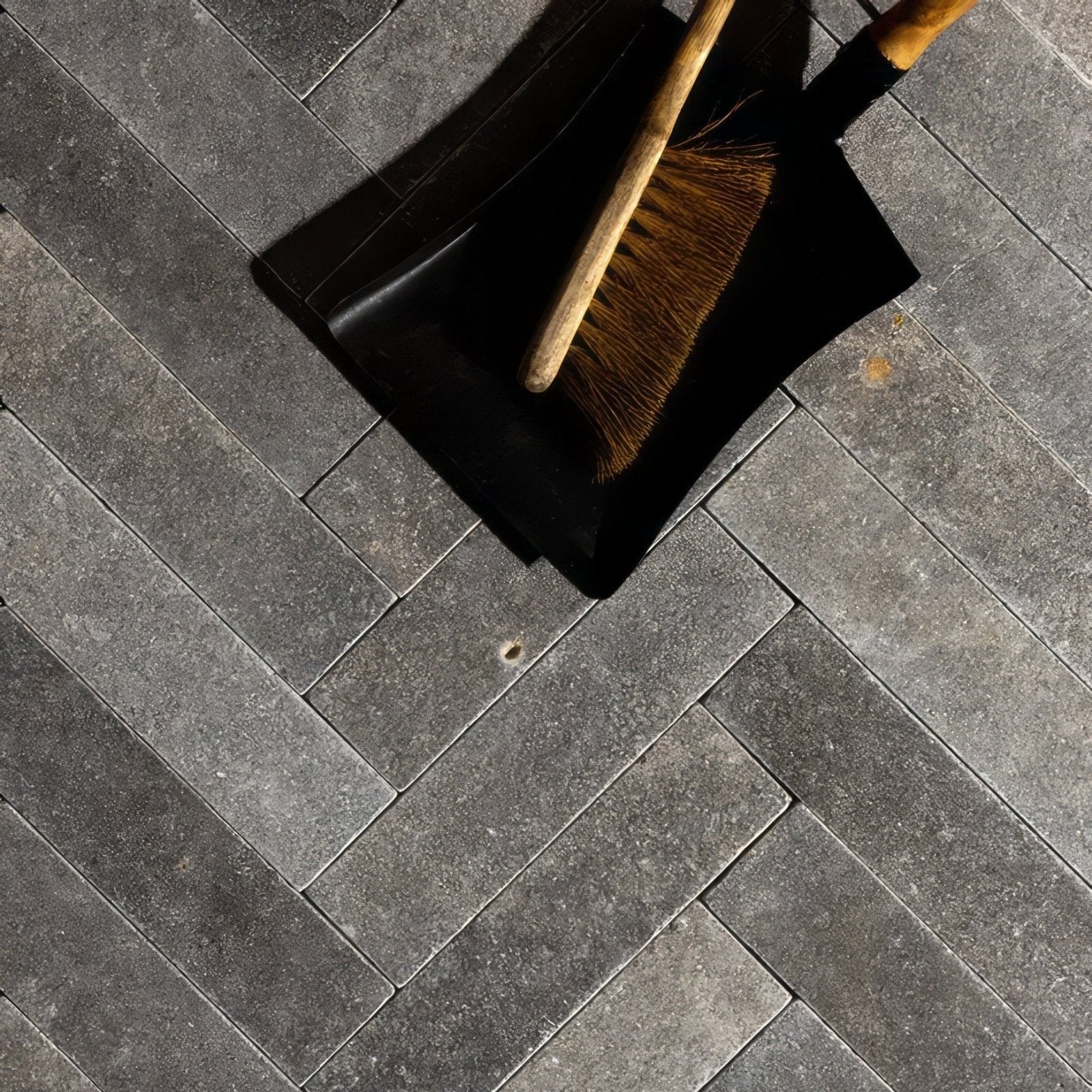 Black plastic dustpan with wooden-handled broom with natural bristles on kimmeridge limestone tumbled and etched parquet