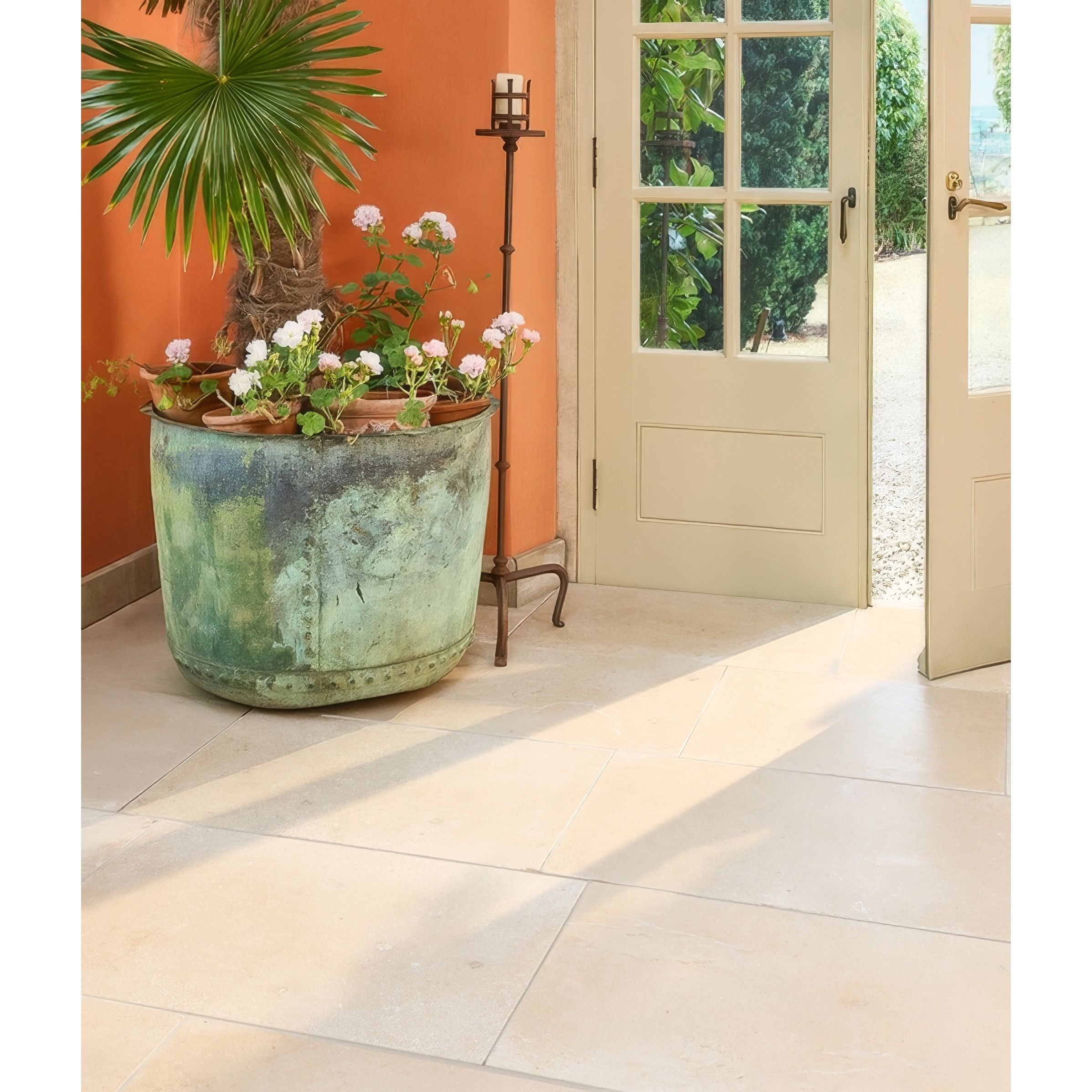 Decorative planter with flowers on a tiled floor in Lacock Tumbled Limestone Flooring next to an open door.