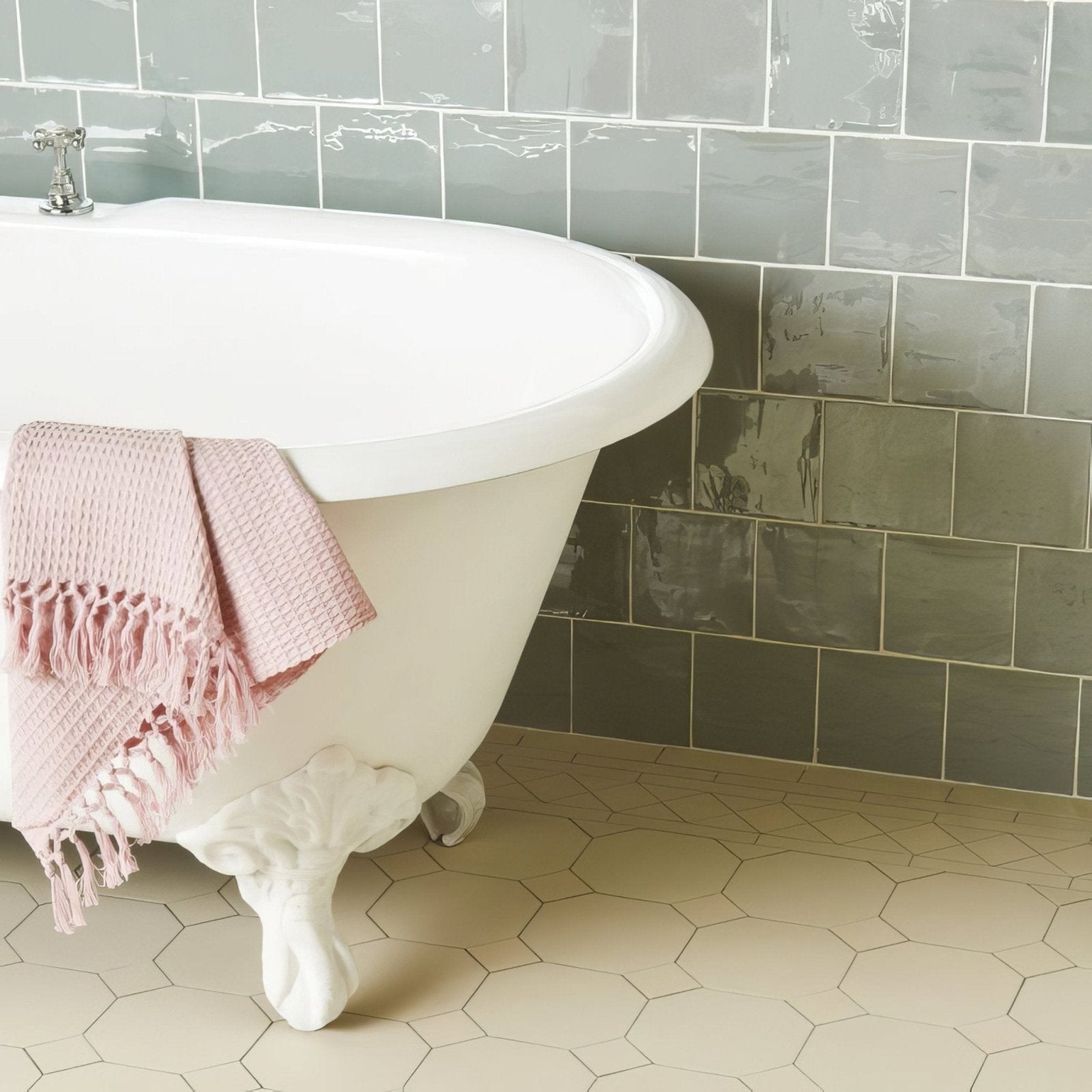 A soft pink waffle-weave towel with delicate fringe hanging over a white clawfoot bathtub in lazul field tile style