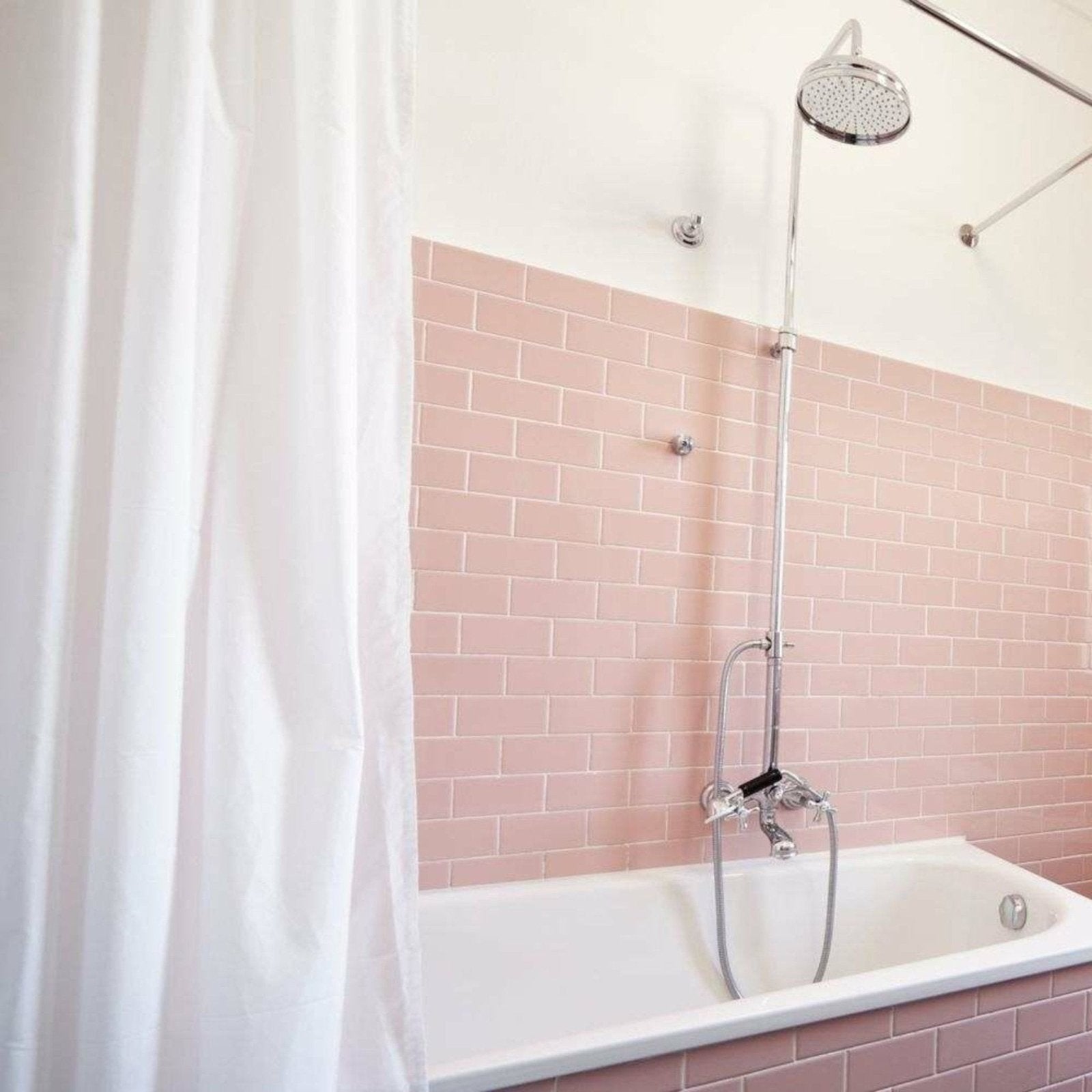 The liso rosa gloss 100x200 bathtub features a sleek white porcelain surface with chrome fixtures on pink subway tiles