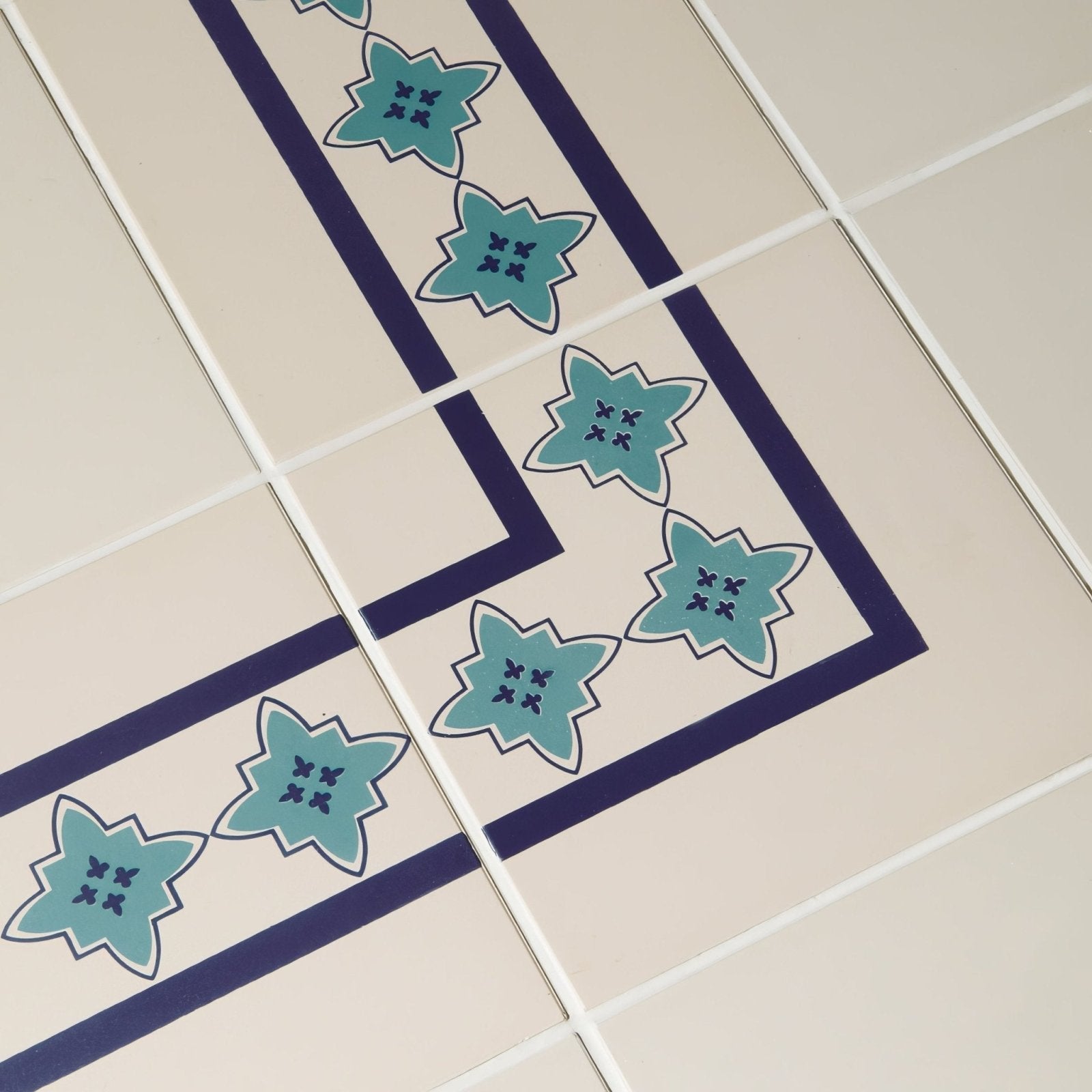 Beige ceramic tiles with a decorative border featuring teal star motifs and navy blue lines called marrakech border dark blue and dark jade on white
