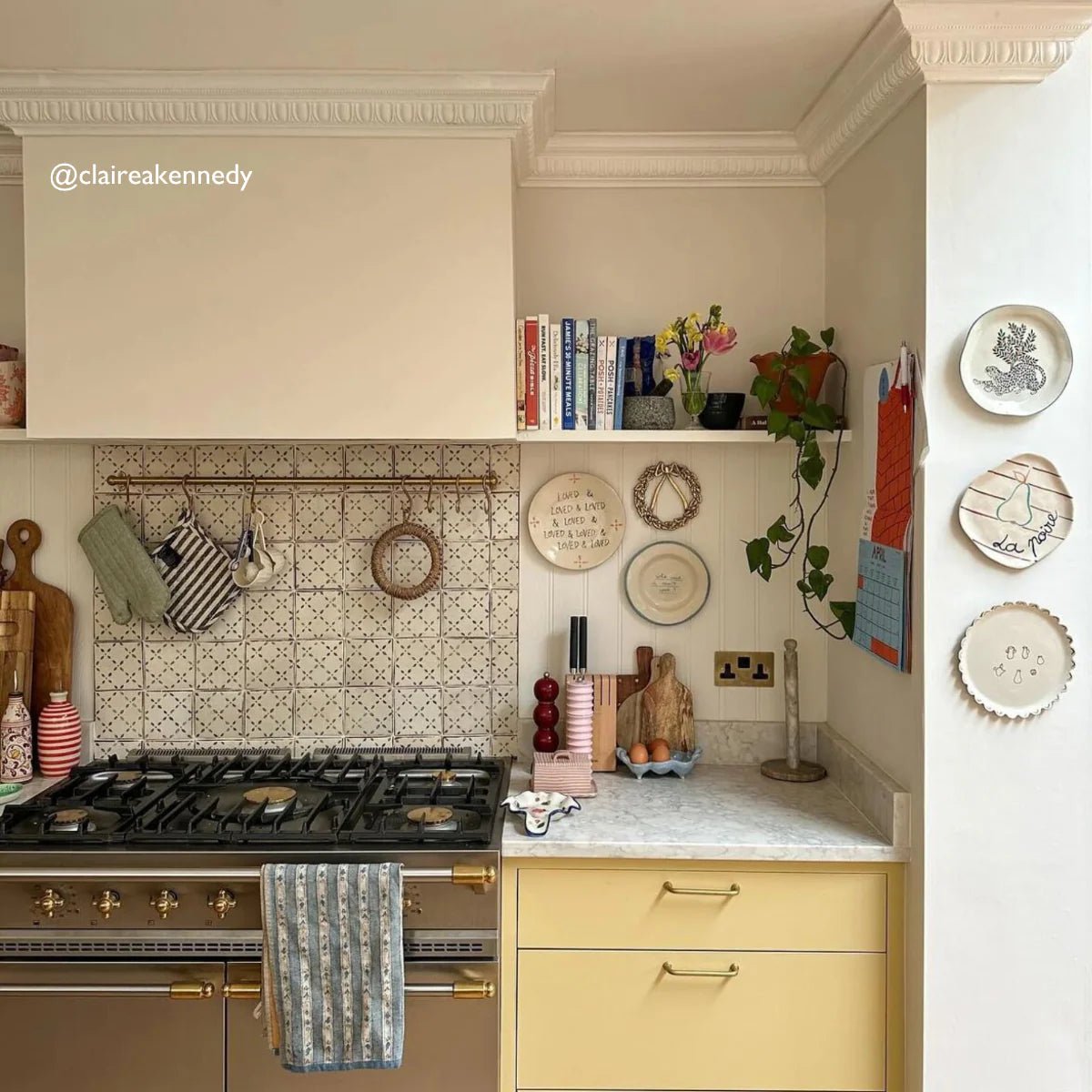Gold-finished range hood with sleek modern design and integrated lighting in front of moroccan patterned terracotta tile wall