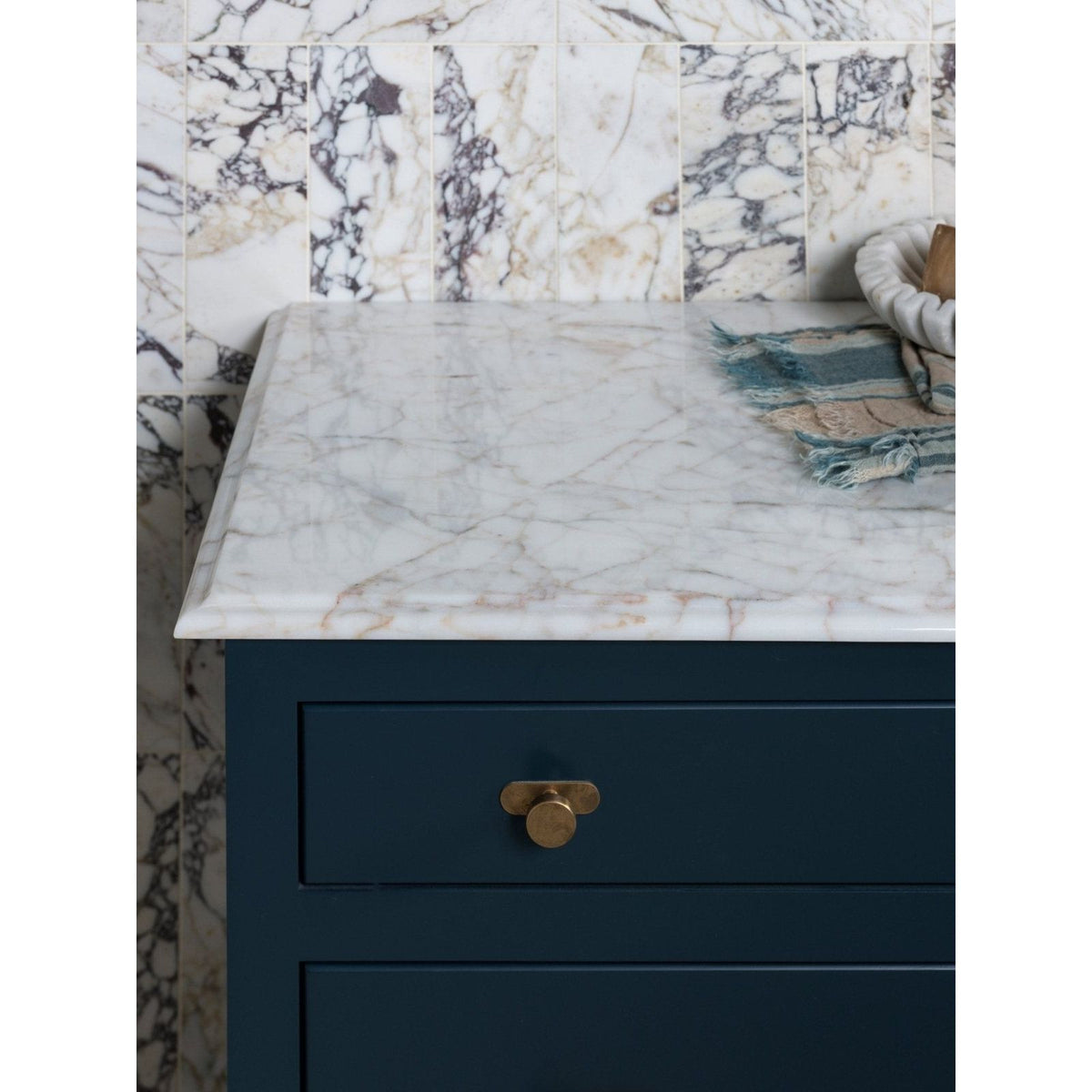 Medici Viola Marble Honed Brick white marble brick tiles with a dark teal cabinet and brass pull