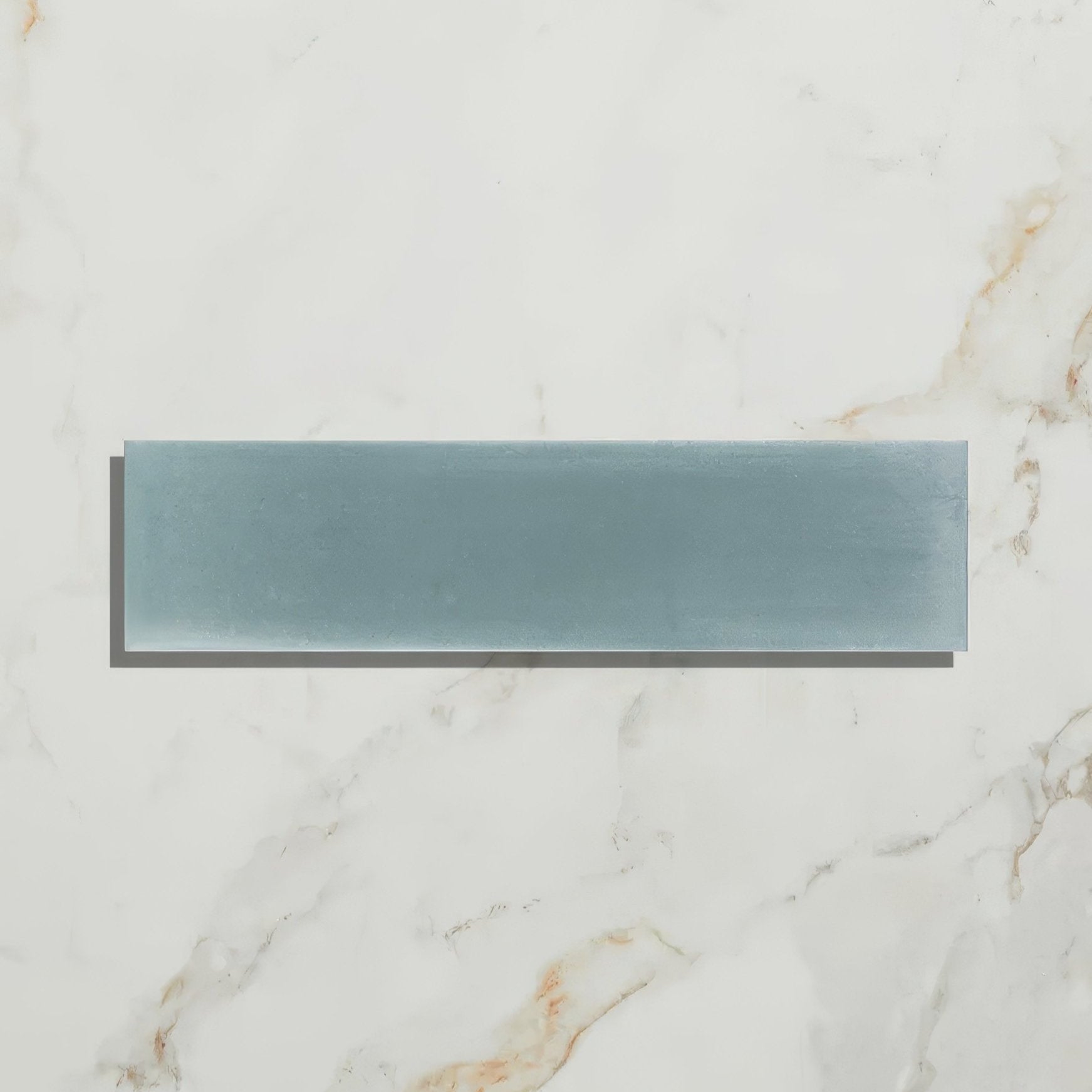 A sleek rectangular teal glass tile with a smooth glossy finish on white marble surface from Medina Brick Porcelain Aqua