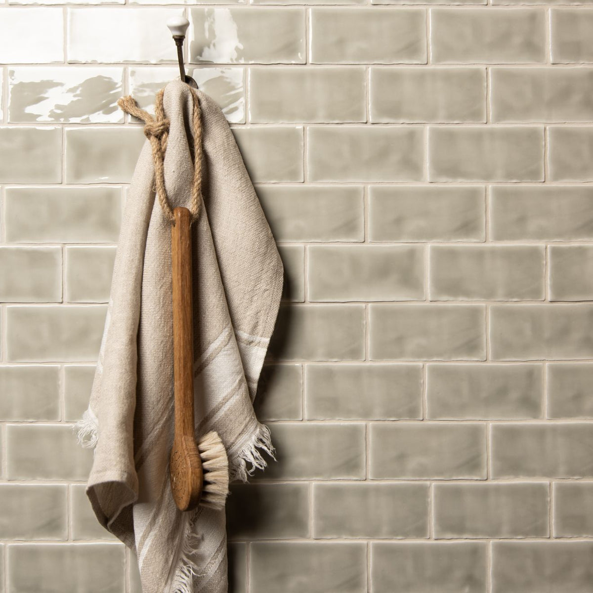 Beige linen towel with frayed edges hanging from wooden-handled brush on mere half tile wall tiles