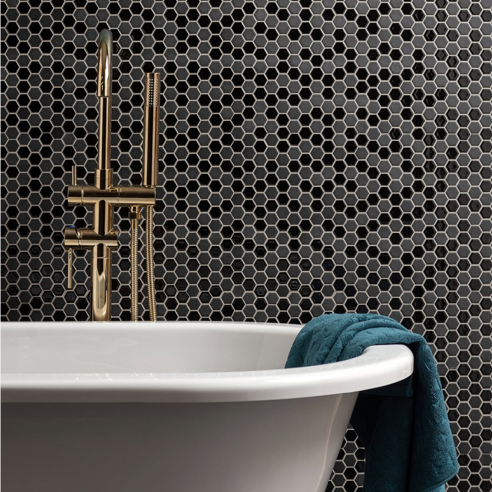 Gold-toned bathtub faucet with sleek modern design against black mixed hexagon mosaic tiles backdrop