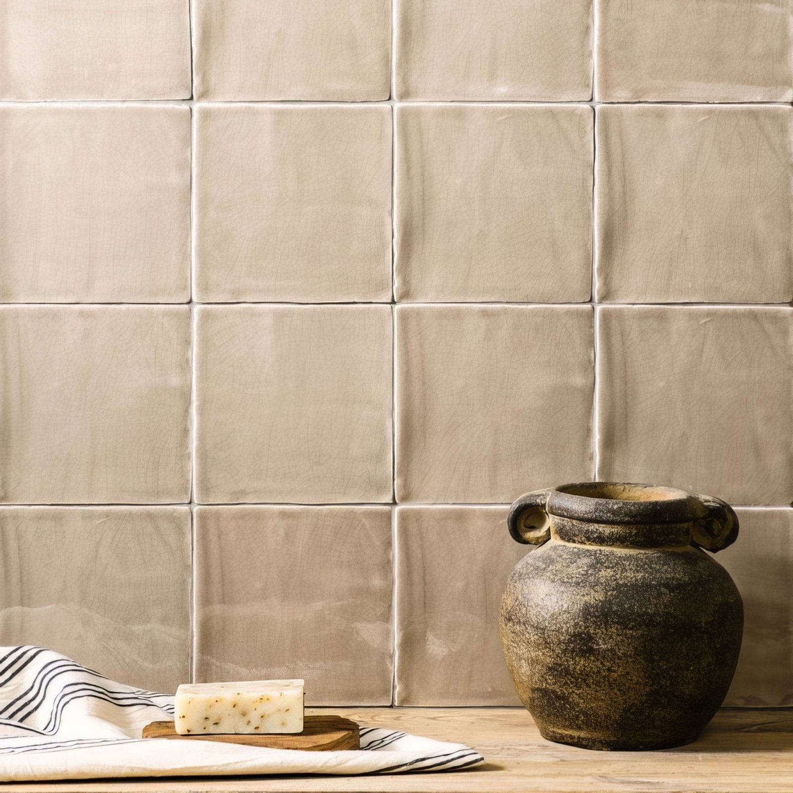 A rustic dark brown ceramic jar with two handles and textured surface on a wooden countertop field tile mink