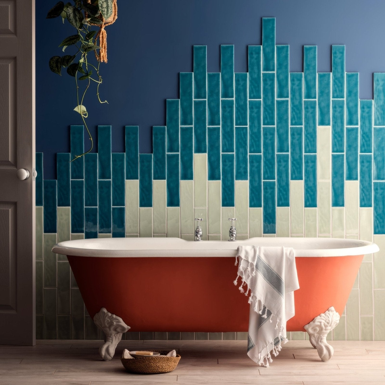 A vibrant coral-colored clawfoot bathtub with white porcelain accents and ornate sculpted feet displayed with mint large brick tile