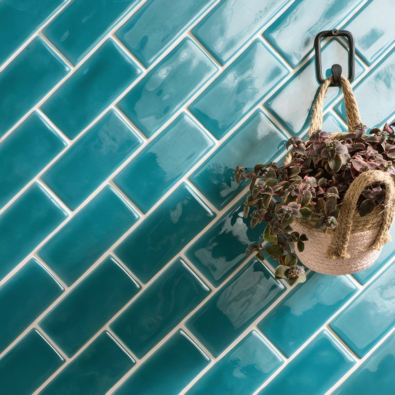 A hanging woven basket with natural fiber handle containing purple and green succulents in moonstone half tile