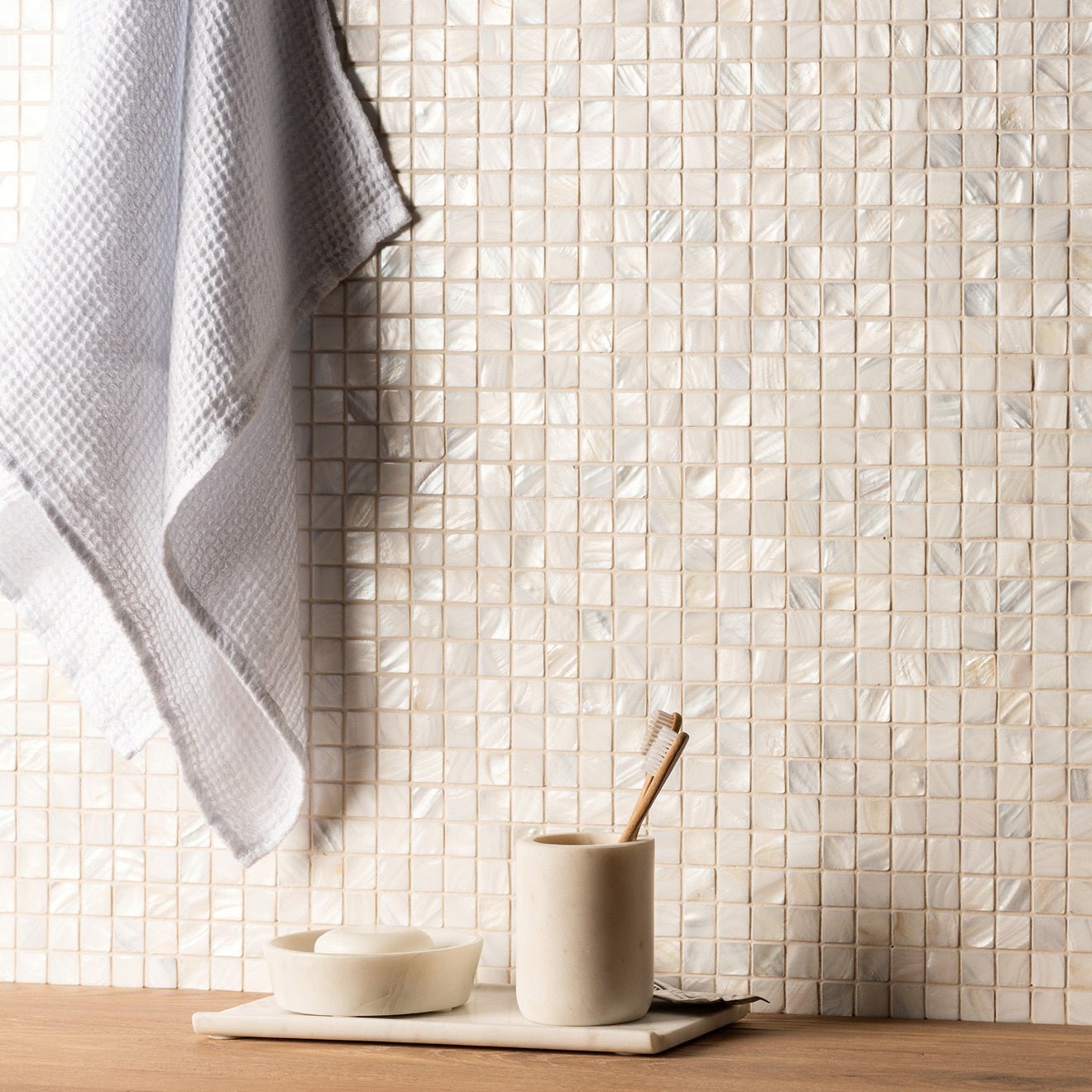 The wall covered in shimmering off-white mother of pearl white square mosaic tiles with an iridescent sheen